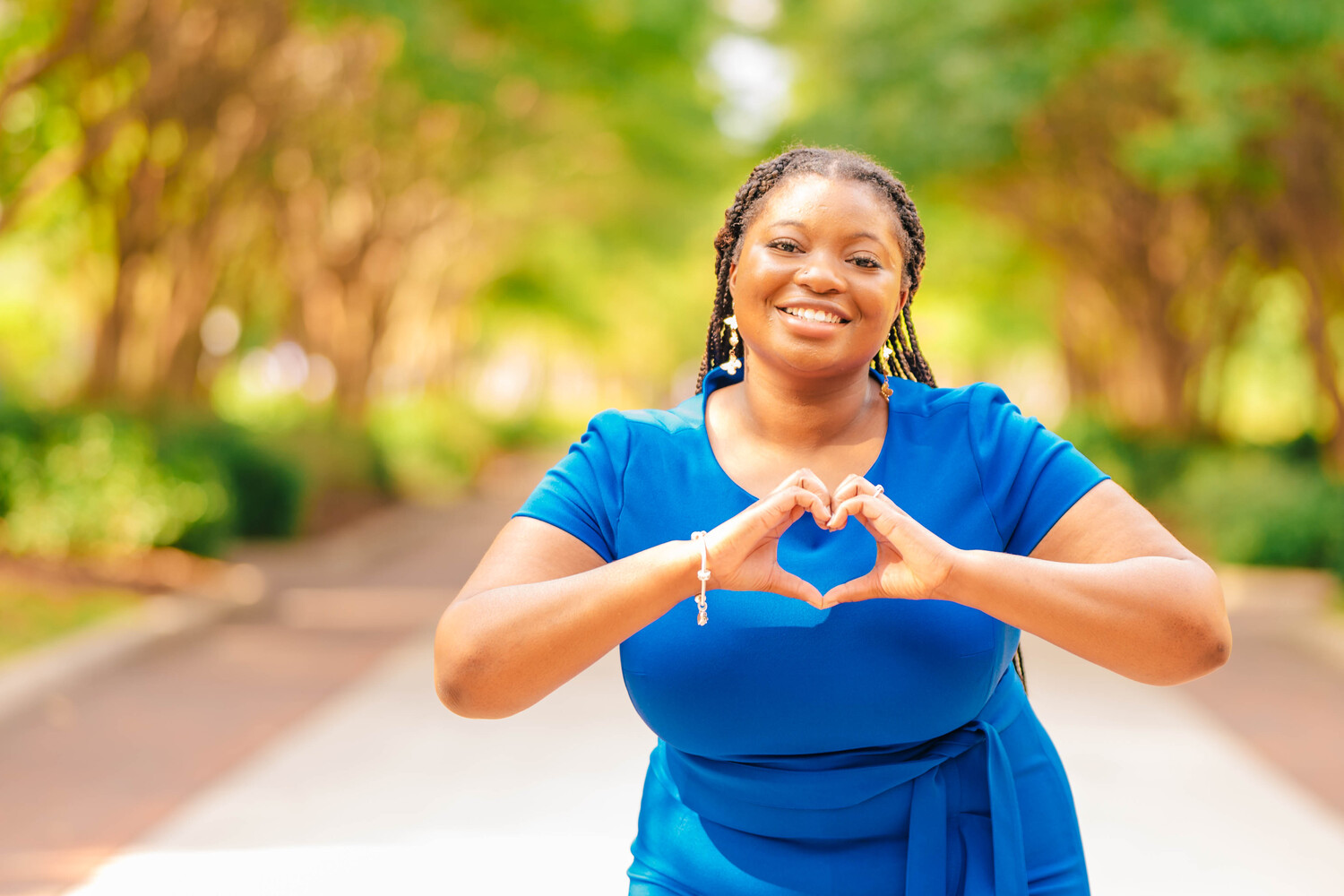 a student dressed in blue, standing in the center of College Avenue and making a "heart" symbol with her hands